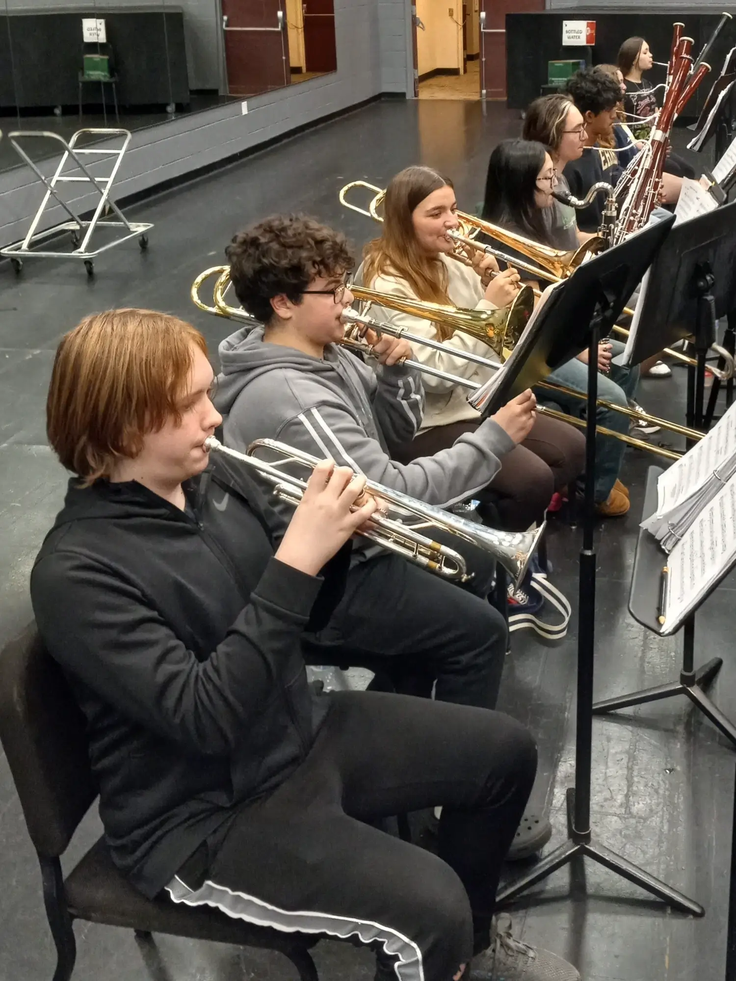 1-15-2025 - Rehearsal photo 6a - Three brass players in the foreground of the back row (cropped)